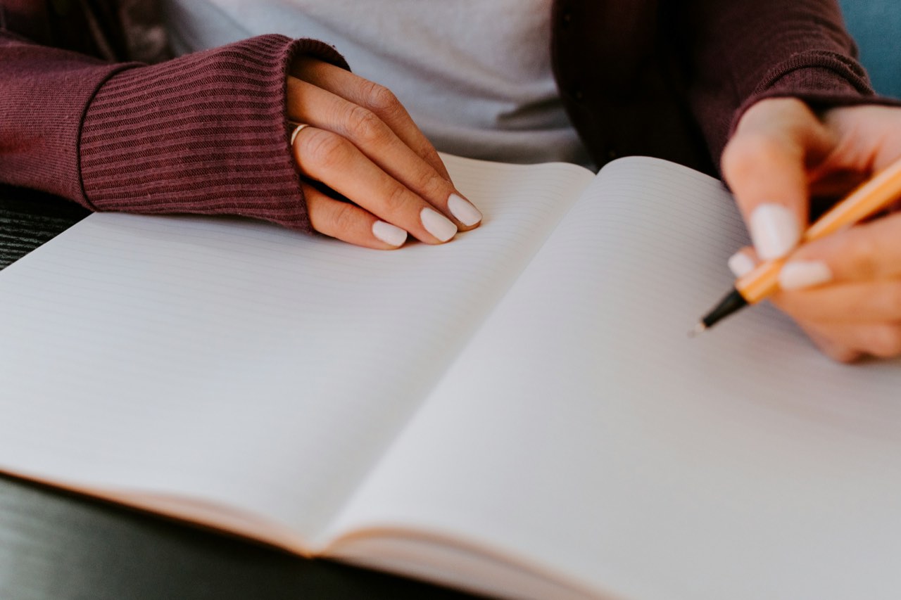 A woman in a burgundy sweater writing in an open, blank notebook.